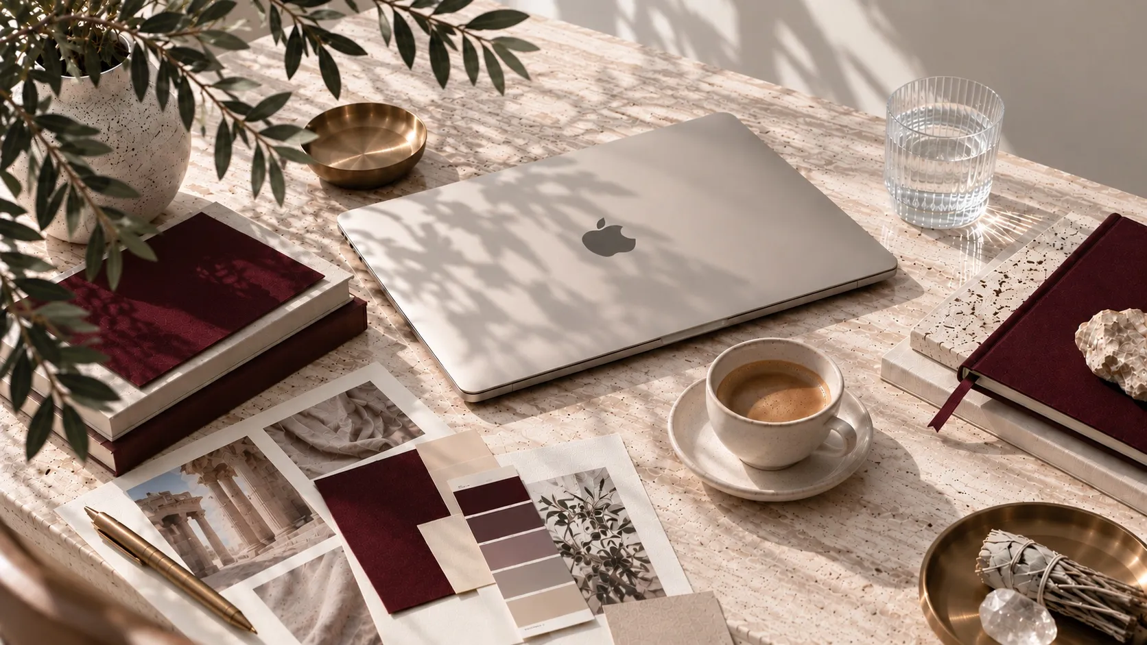Desk with a laptop, coffee, color swatches and burgundy notebooks in natural light