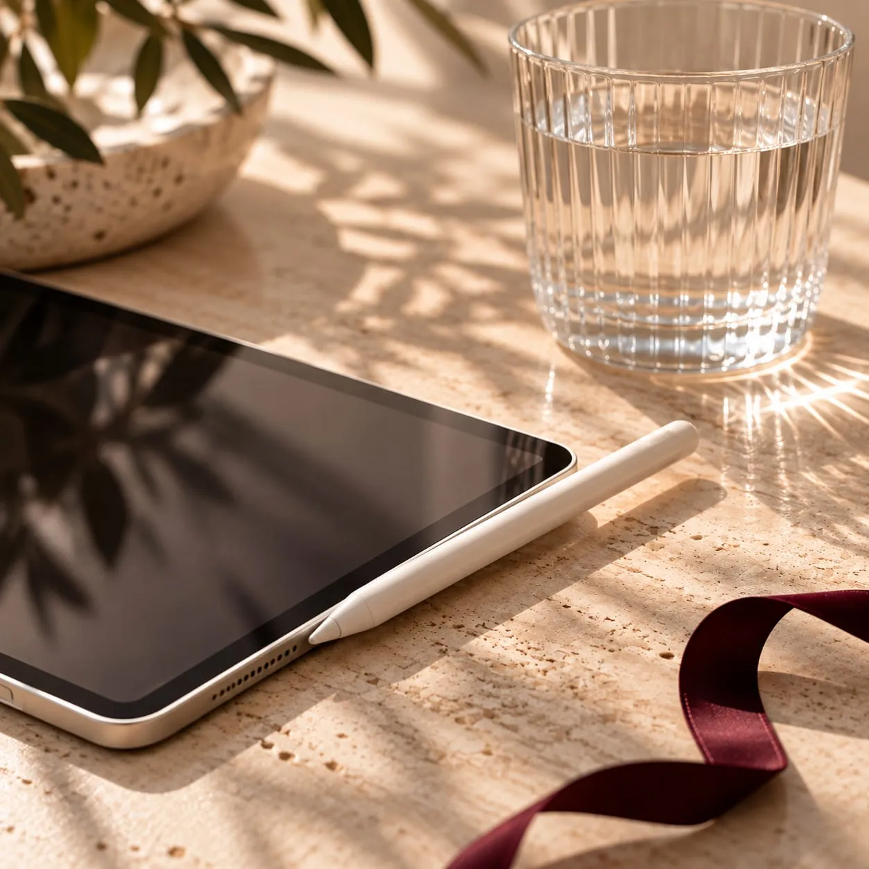 Tablet with a digital pencil, a glass and a burgundy ribbon on a table